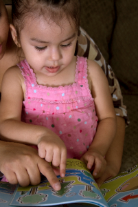 Parent reading to young girl pointing at pictures